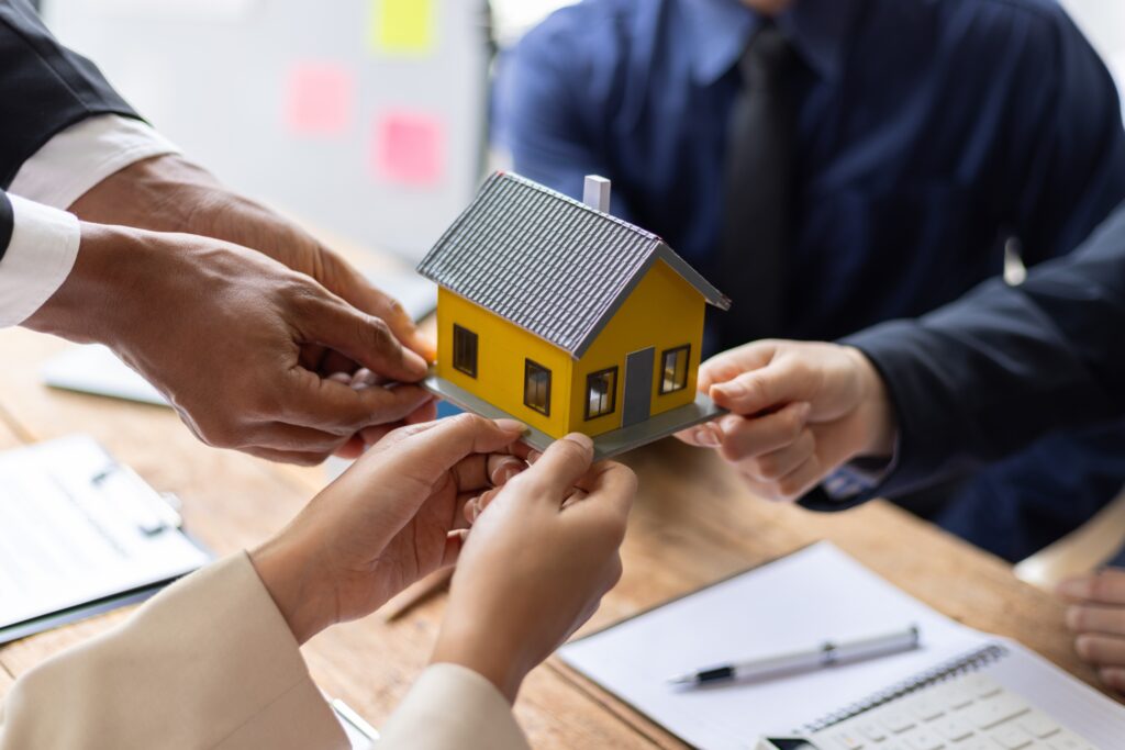 Real estate agents are holding a miniature house model during a meeting, property sales, investment, and homeownership.